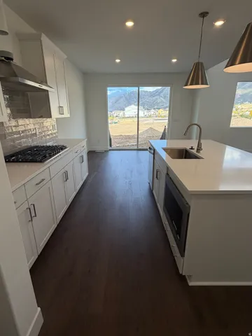 White kitchen cabinetry with stainless steel appliances, a center island with sink and pendant lighting, wood-finish flooring, and a sliding glass door