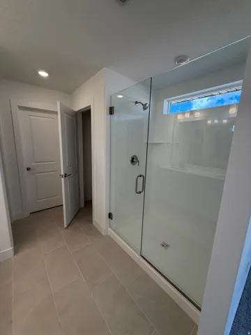 Owner's Bath spacious shower with a glass enclosure, tiled flooring, and modern lighting