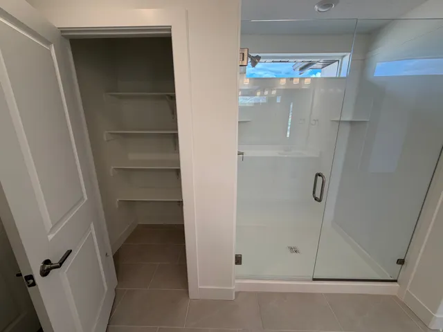 Walk-in shower with clear glass enclosure, integrated shelving, and transom window