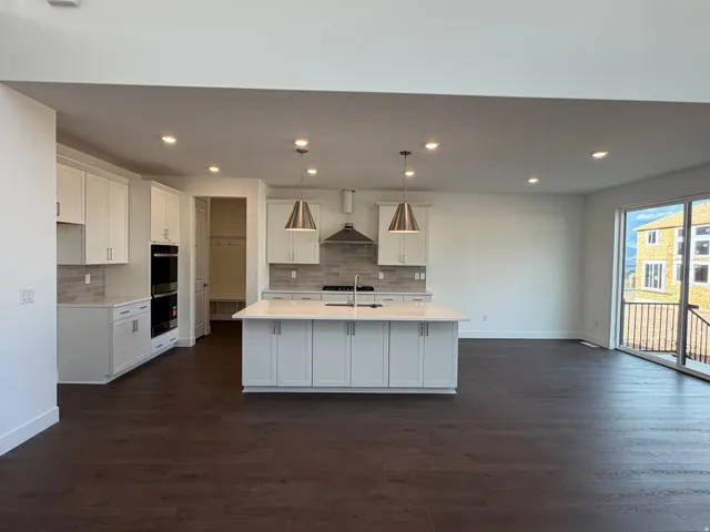 Open-concept kitchen with white shaker cabinetry, an expansive central island, stainless steel double wall ovens, and wood-finish flooring