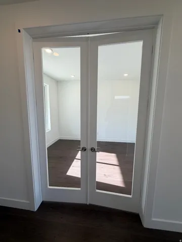 White French doors with clear glass panels, contemporary brushed nickel hardware, dark wood-finish flooring, recessed lighting, and a white interior