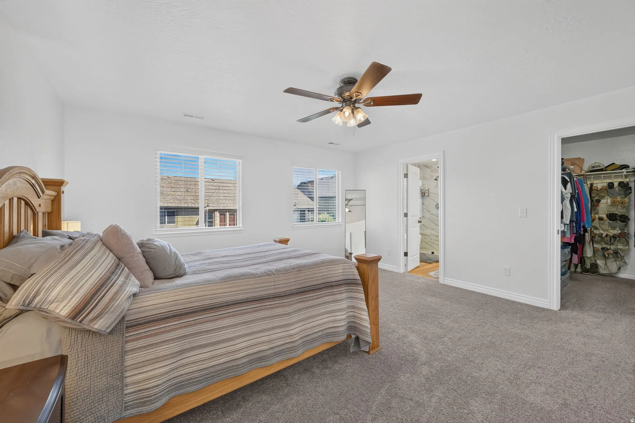 Carpeted room with a ceiling fan, two windows with blinds, and two doorways, one opening to a walk-in closet and the other to a bathroom