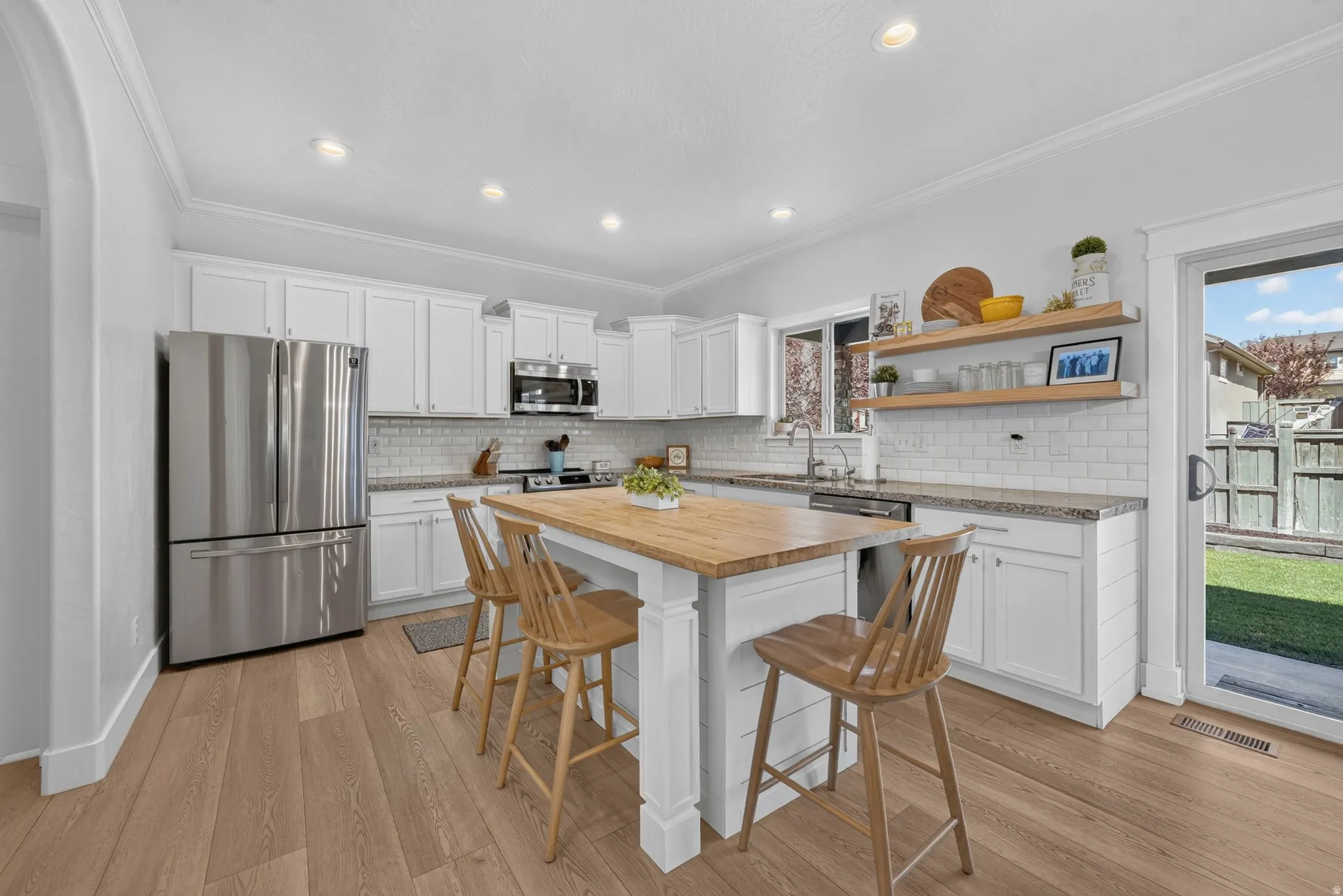 Kitchen featuring wood-finish flooring, white cabinetry, granite countertops, subway tile backsplash, a central island with a wood countertop, and stainless steel appliances