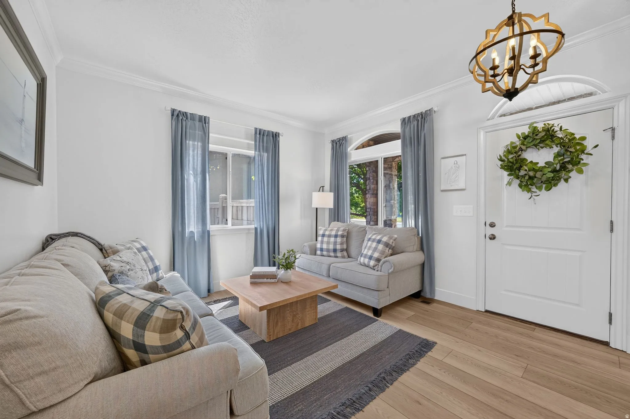 Entryway and living area featuring wood-finish flooring, crown molding, a decorative ceiling light fixture, and a white paneled entry door with an arched transom window