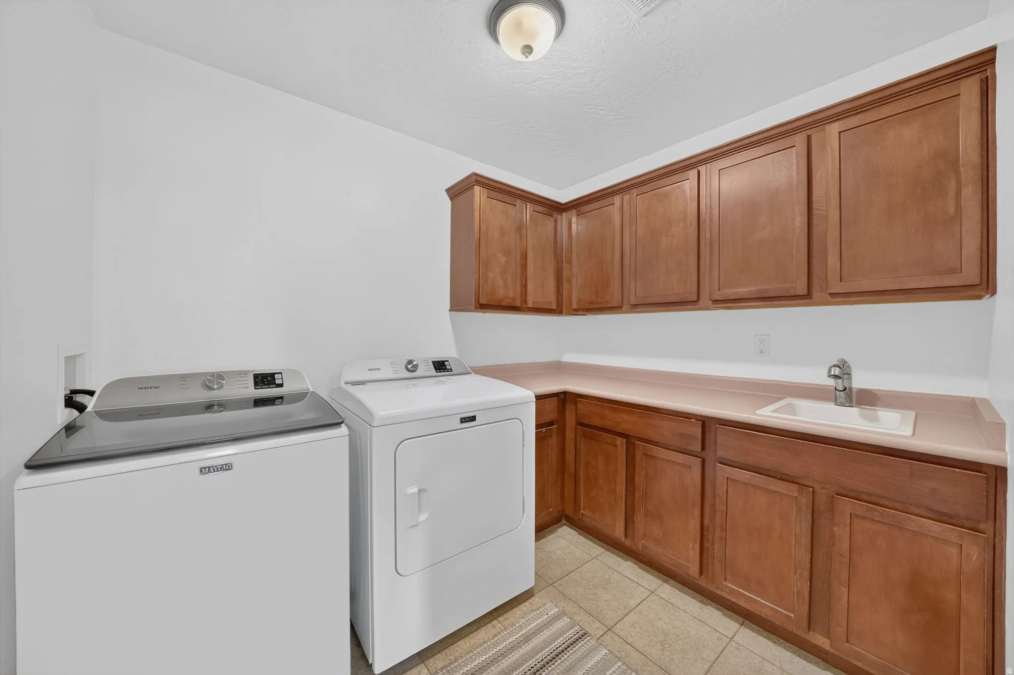 Utility room featuring wood-finish cabinetry, a built-in sink, a light-toned countertop, and tiled flooring