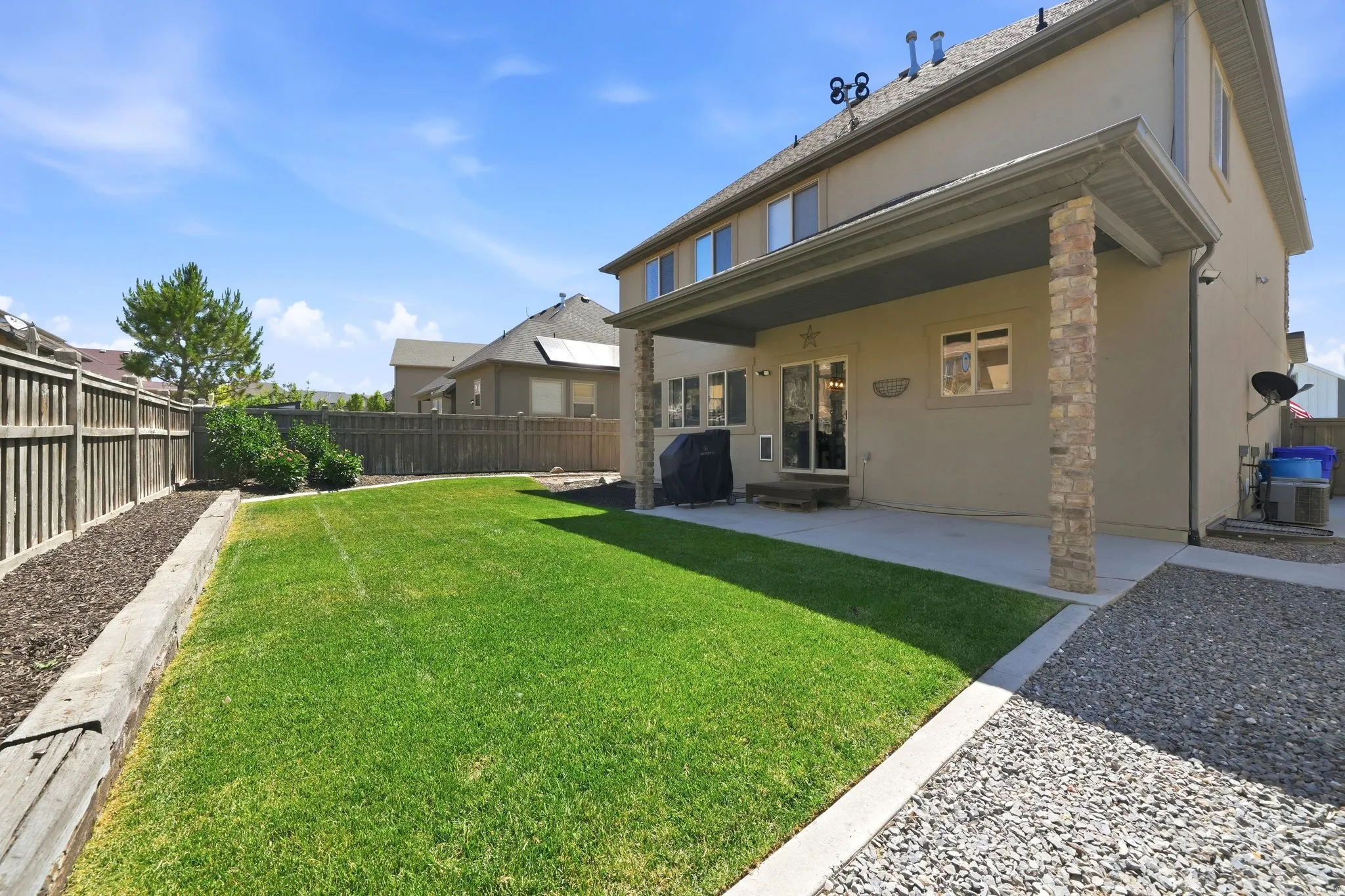 Expansive backyard featuring a manicured lawn, full privacy fencing, and a covered patio supported by stone-clad columns