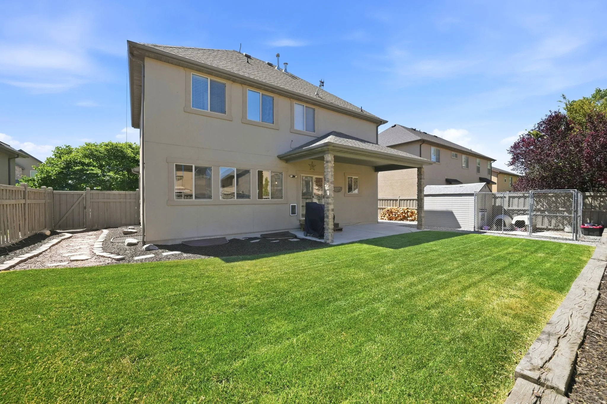 Expansive rear yard featuring a manicured lawn, covered patio, stone pathway, full fencing, and a storage shed