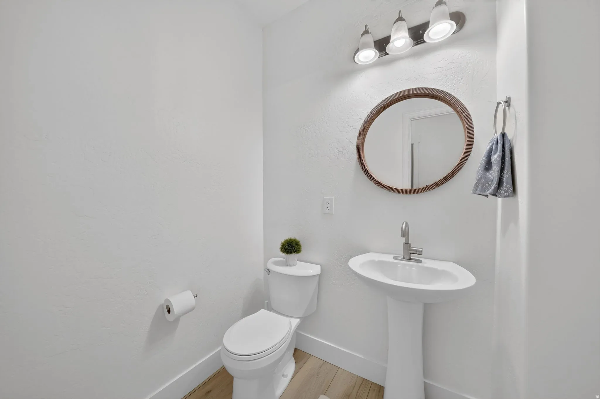 Pedestal sink with brushed nickel faucet, an oval framed mirror, and a three-light vanity fixture