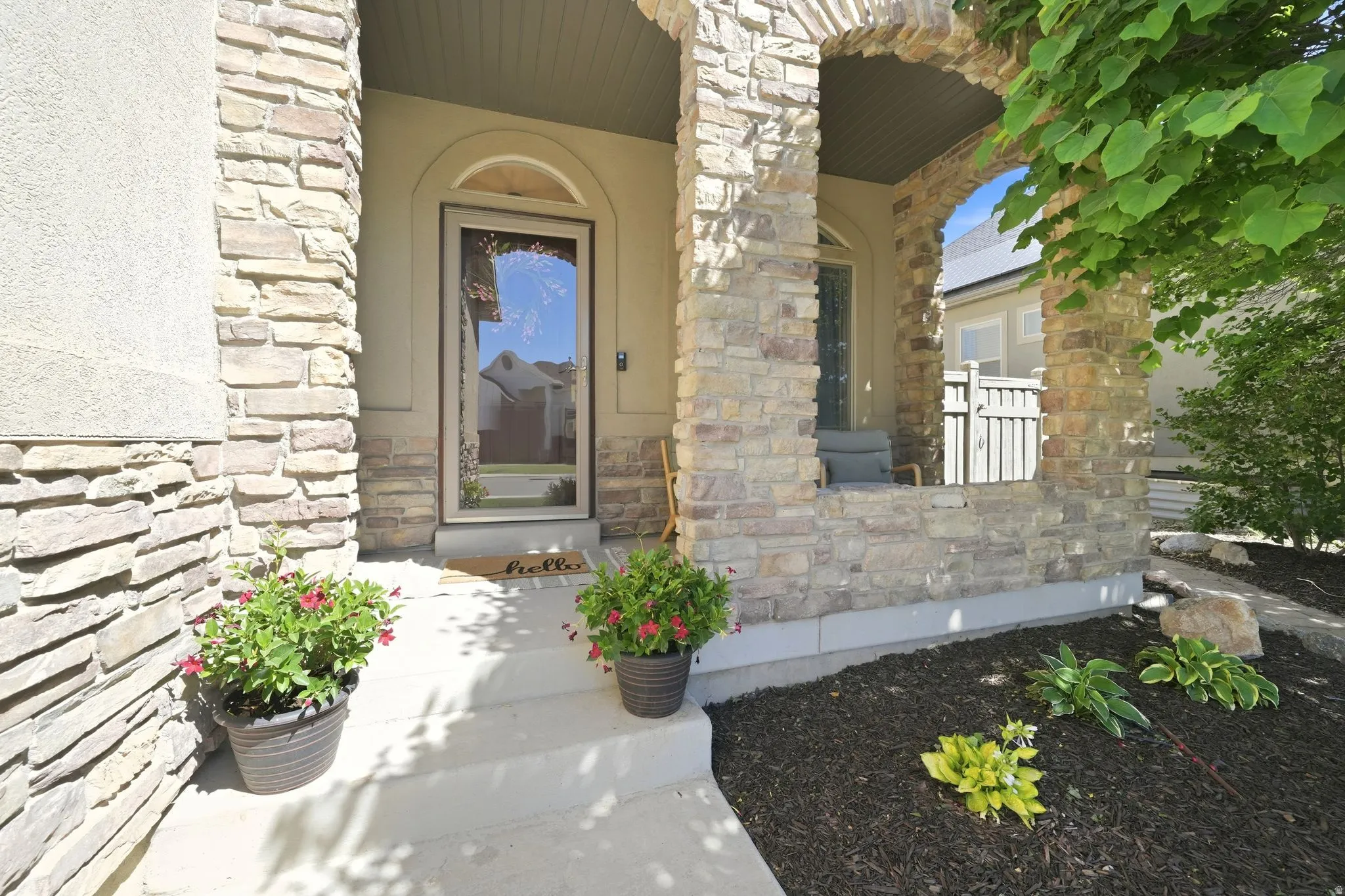 Stone-clad entry featuring an arched stone portico, stucco accents, concrete steps, a full-light entry door, and landscaped planting beds