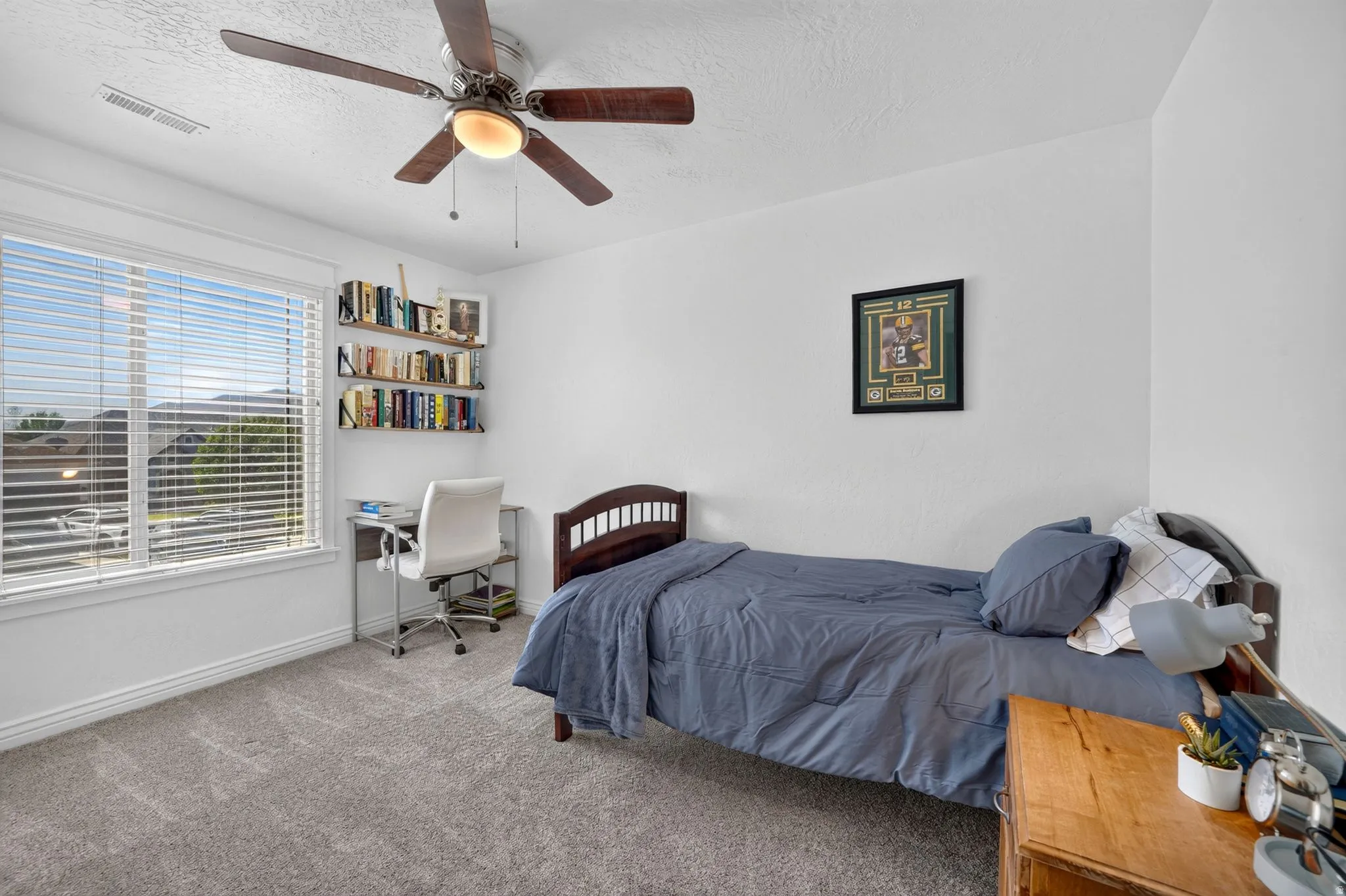 Bright room featuring a large window with blinds, a ceiling fan with light fixture, built-in shelving, and neutral carpeting