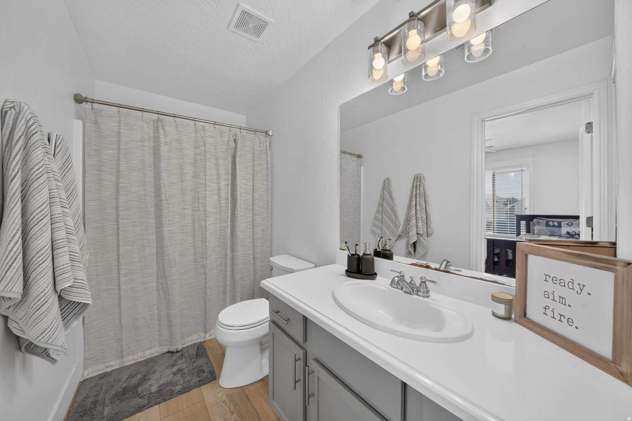 Bathroom featuring wood-finish flooring, a white vanity countertop, gray cabinetry, and a shower/tub combination with a chrome shower rod