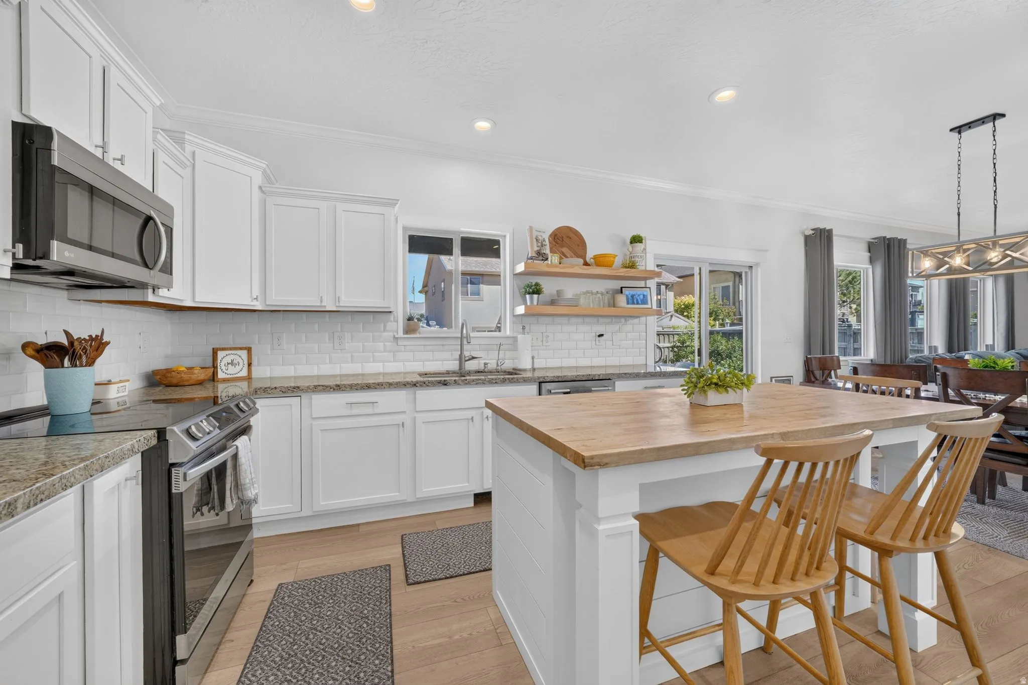 Open-concept kitchen featuring an oversized island with a wood-finish countertop, white shaker-style cabinetry, stainless steel appliances, and a subway tile backsplash