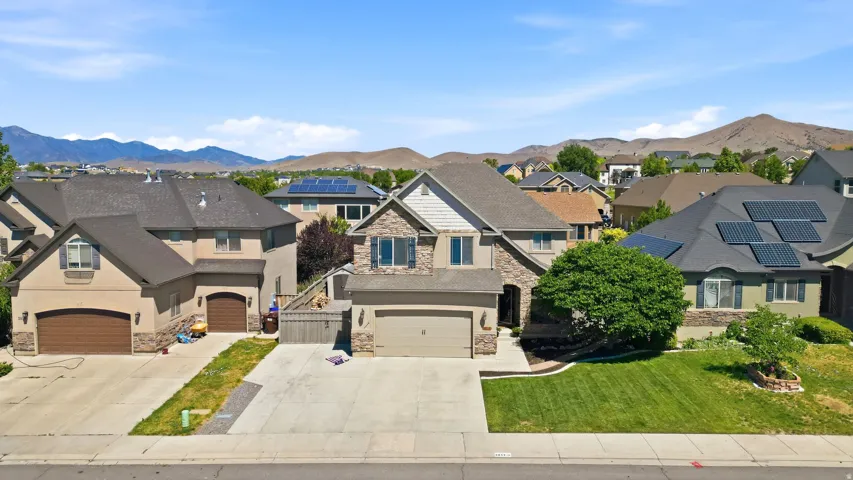 Two-story residence featuring a stone and stucco exterior, an attached garage, a front lawn with mature landscaping, a paved driveway, and mountain scenery