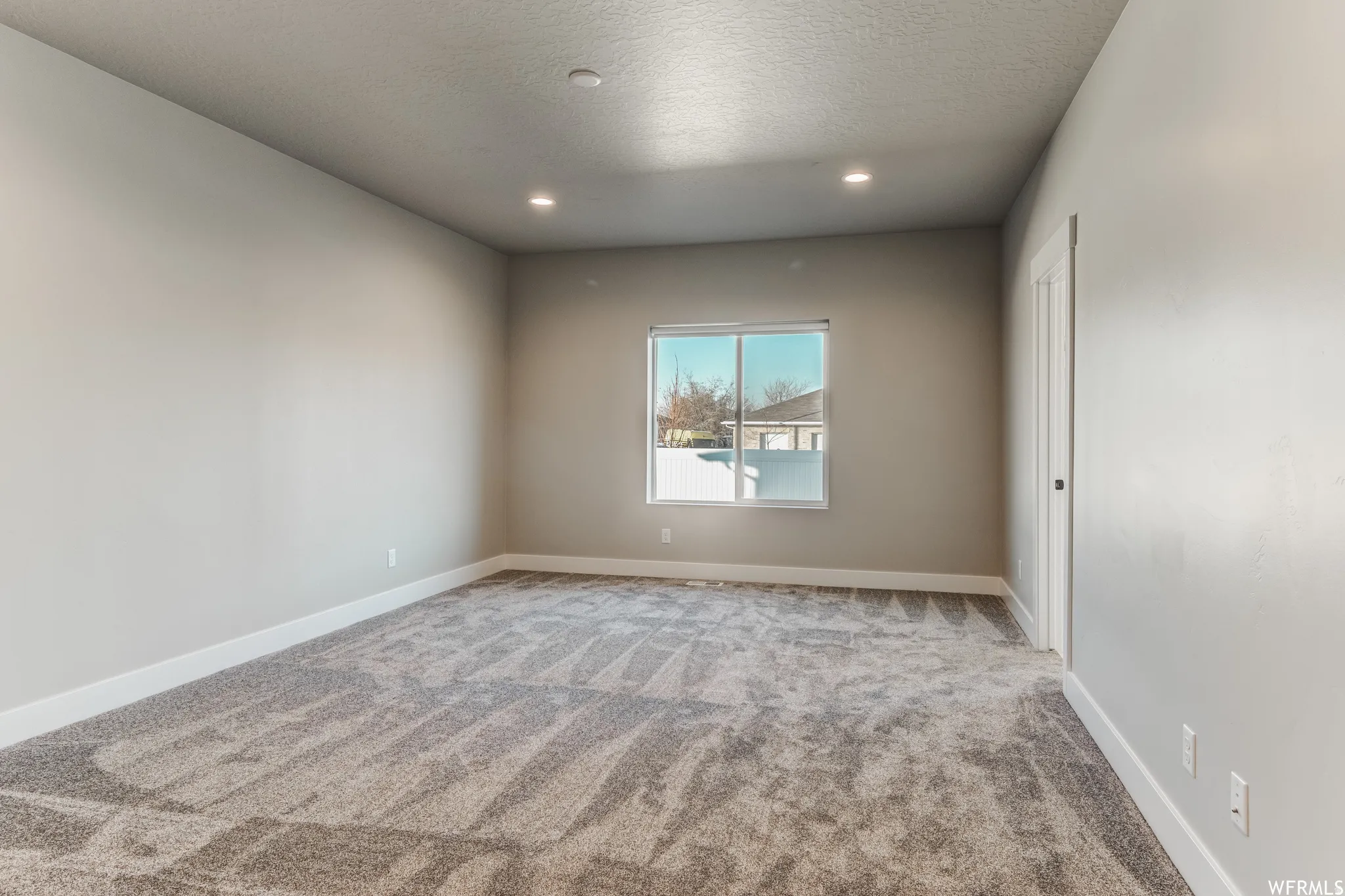 Recessed lighting, neutral wall paint, gray patterned carpeting, white trim, and a bright window