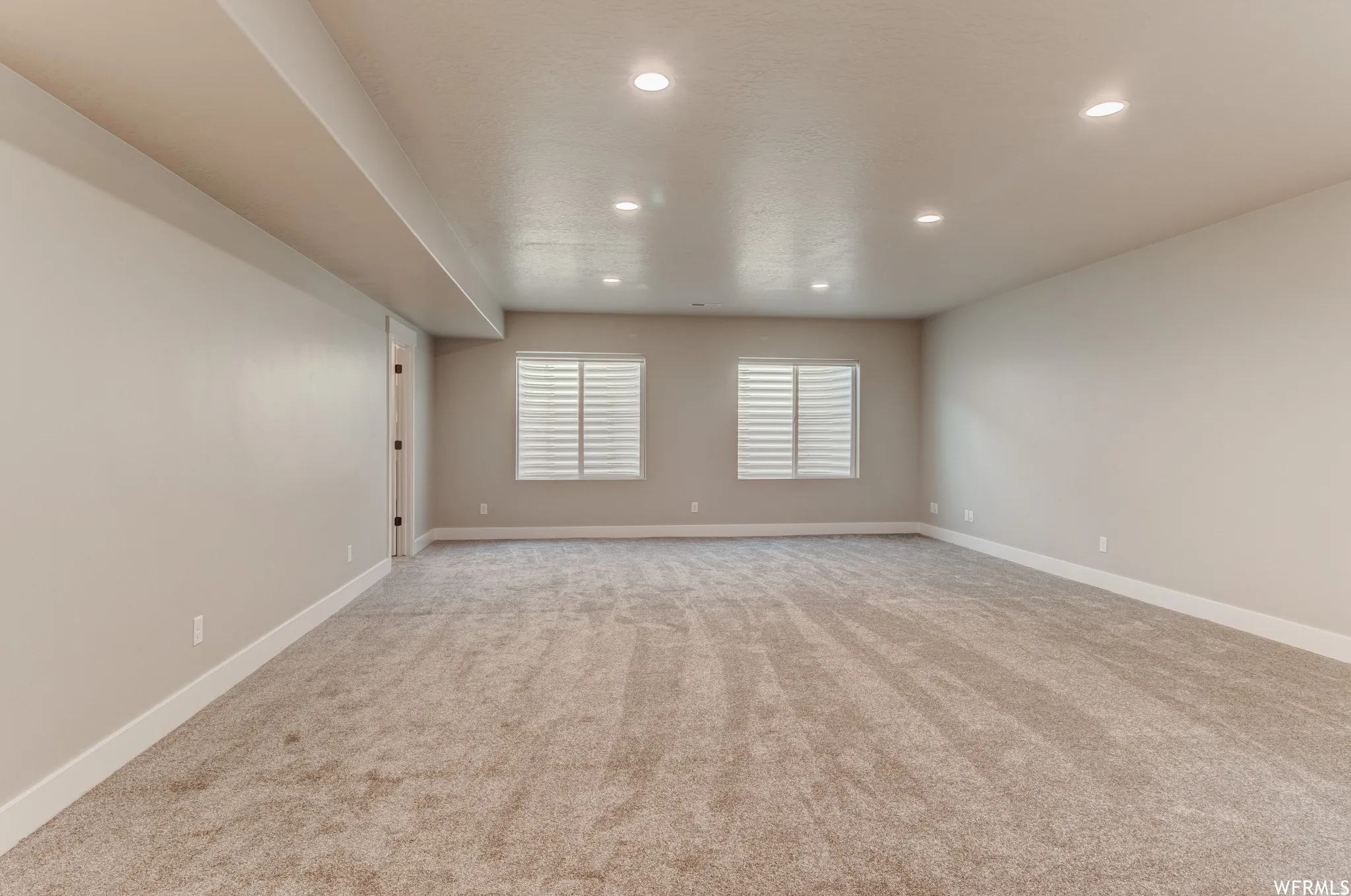 Spacious room featuring neutral carpeting, recessed lighting, and two windows with horizontal blinds