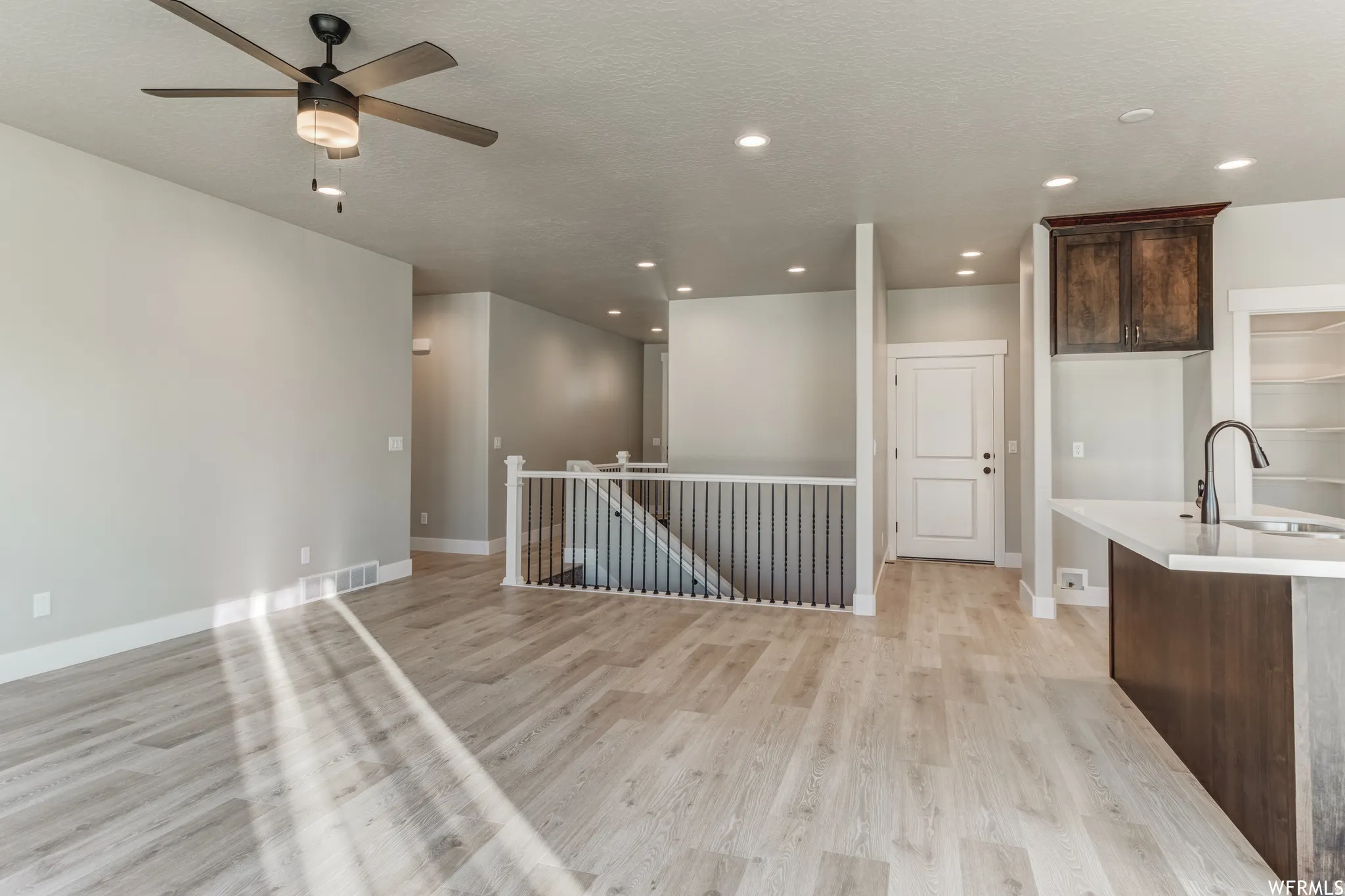 Open-concept living space with wood-finish flooring, a contemporary ceiling fan, recessed lighting, and a kitchen island with a built-in sink and dark cabinetry