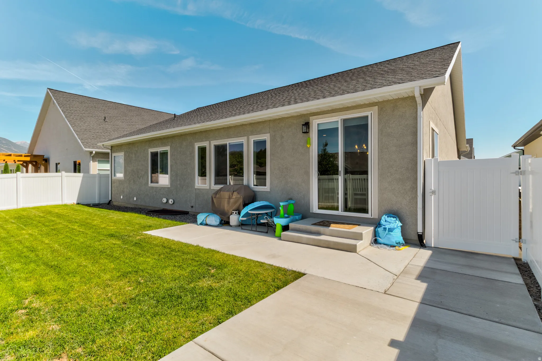 Rear exterior featuring a concrete patio, sliding glass door entry, multiple windows, a white vinyl fence, and a manicured lawn