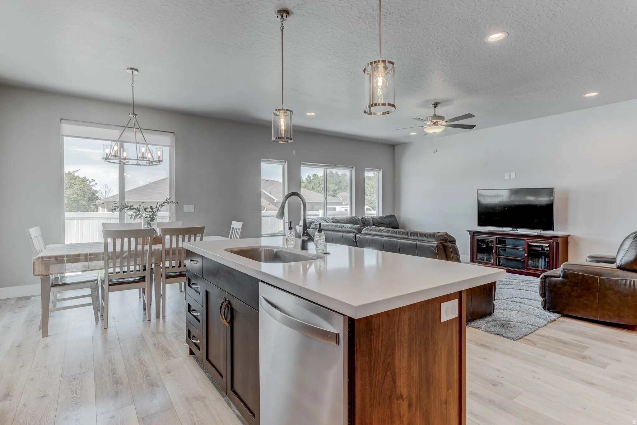 Open-concept living space featuring wood-finish flooring, a kitchen island with integrated sink, recessed lighting, and a ceiling fan