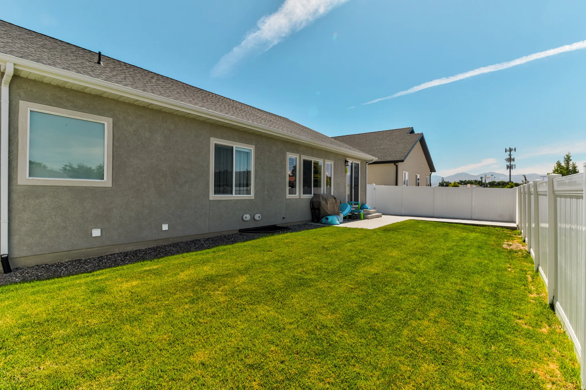 Spacious backyard with a vibrant green lawn, concrete patio, and white privacy fencing