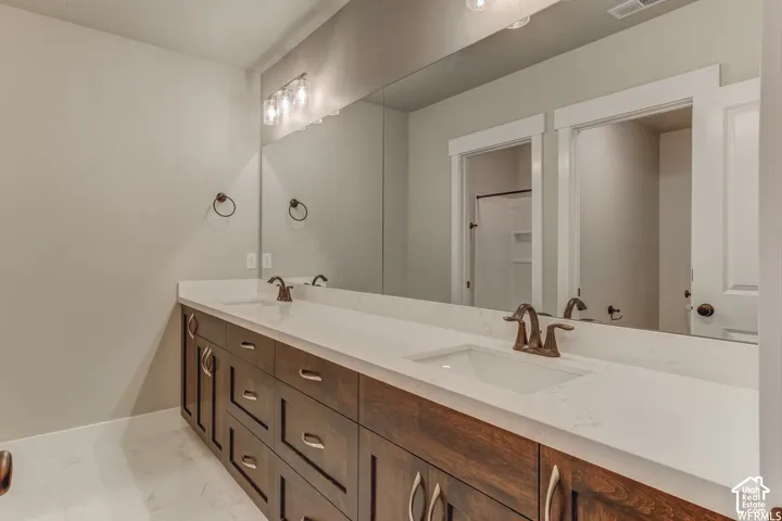 Dual vanity with integrated sinks, expansive mirror, wood-finish cabinetry, and contemporary bronze fixtures