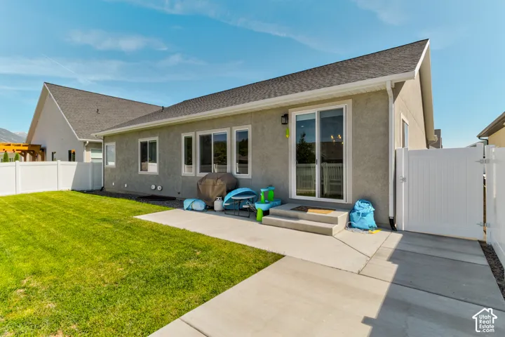 Rear exterior featuring a concrete patio, sliding glass door entry, multiple windows, a white vinyl fence, and a manicured lawn