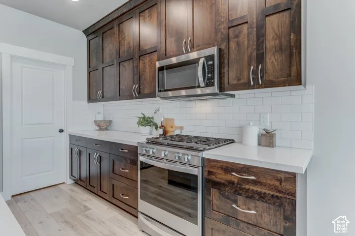 Kitchen featuring dark wood cabinetry, light countertops, white subway tile backsplash, stainless steel range with gas cooktop, and an over-the-range microwave