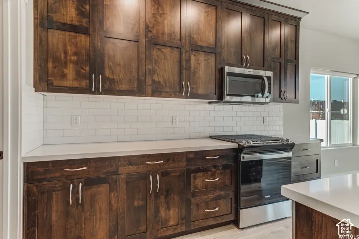 Dark wood-finish cabinetry with silver hardware, white subway tile backsplash, white countertops, stainless steel microwave, and stainless steel range