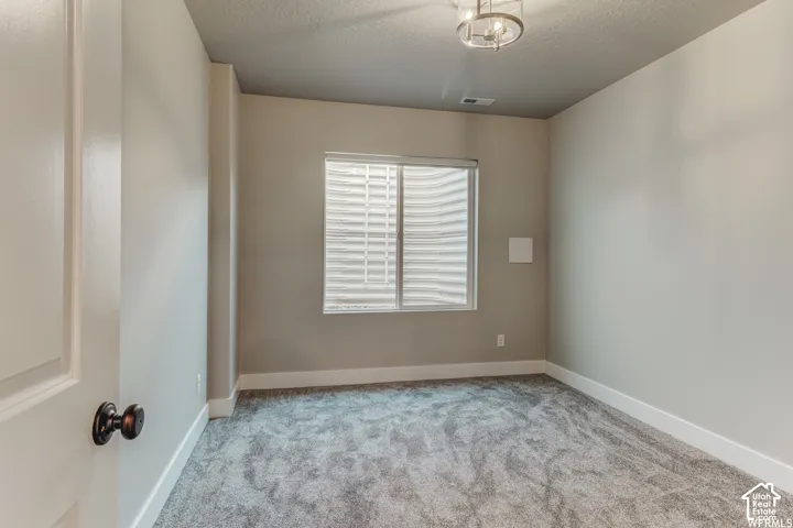 Neutral tone walls, gray carpet flooring, white trim, window with blinds, and a modern ceiling fixture