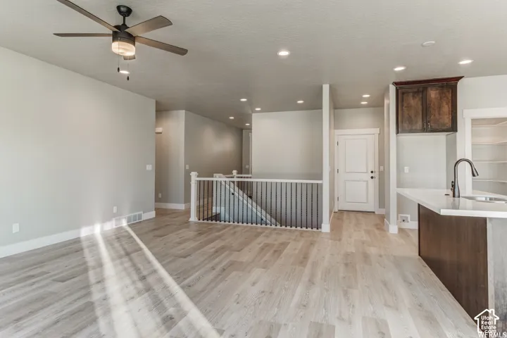 Open-concept living space with wood-finish flooring, a contemporary ceiling fan, recessed lighting, and a kitchen island with a built-in sink and dark cabinetry