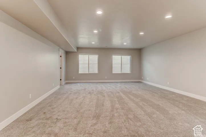Spacious room featuring neutral carpeting, recessed lighting, and two windows with horizontal blinds