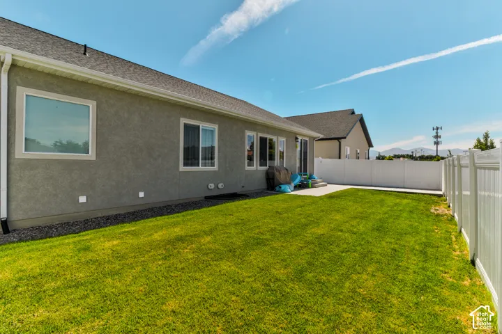 Spacious backyard with a vibrant green lawn, concrete patio, and white privacy fencing