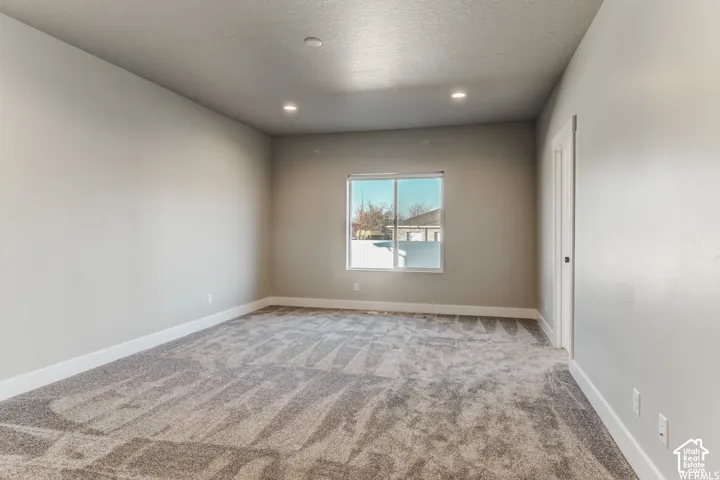 Recessed lighting, neutral wall paint, gray patterned carpeting, white trim, and a bright window