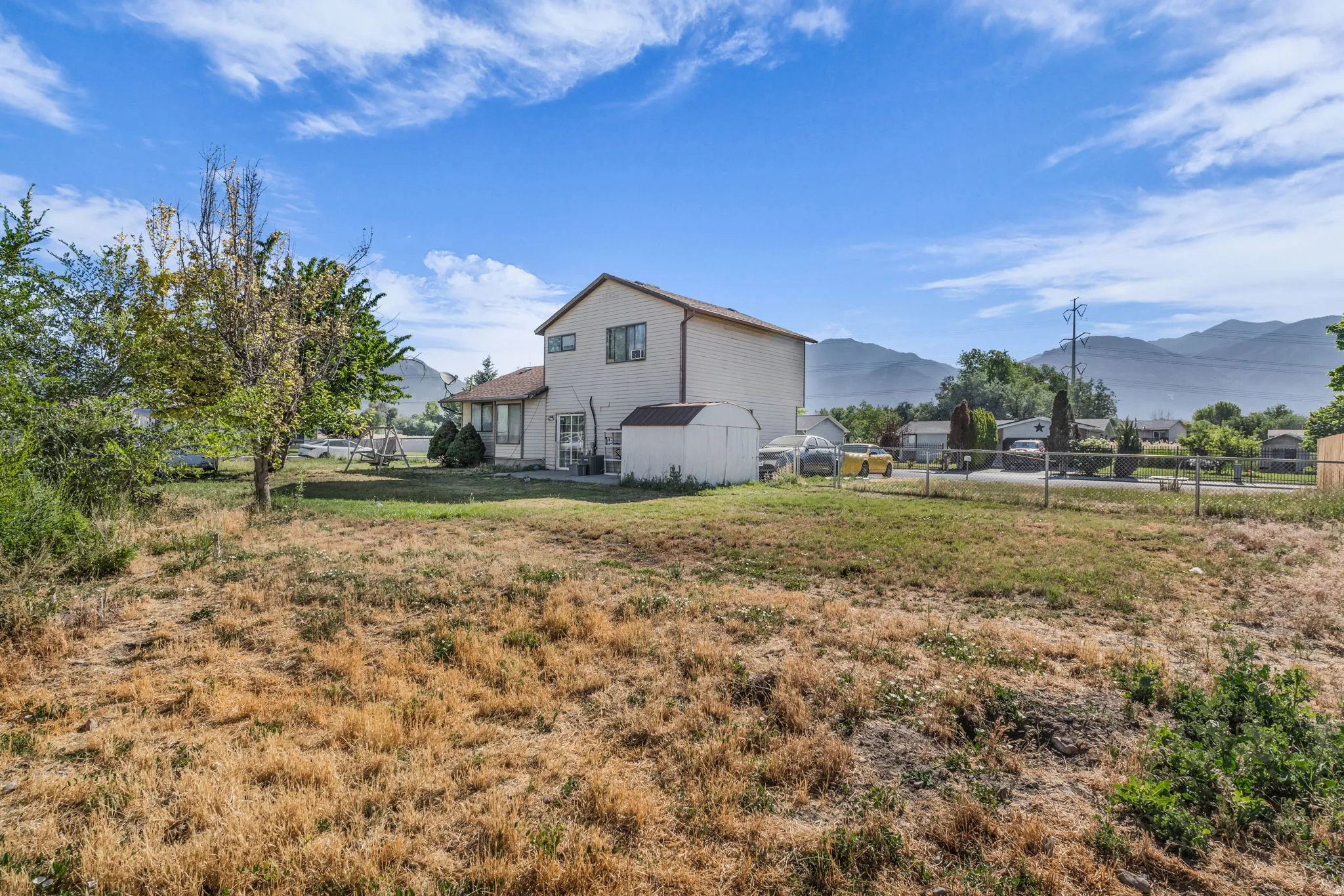 Expansive rear lot featuring a residential structure, mature trees, and a utility shed