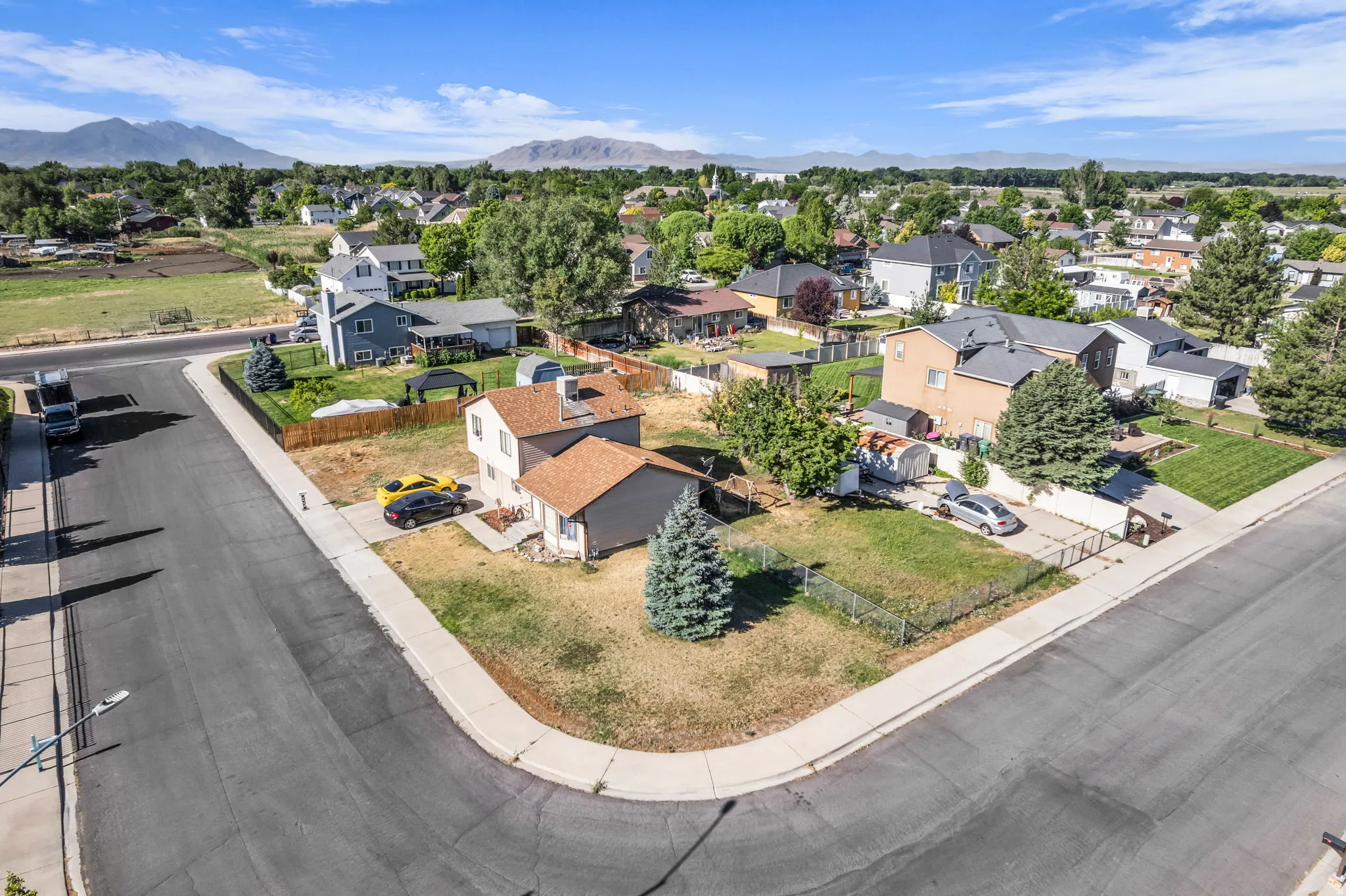 Corner lot property featuring a detached garage, mature trees, and a concrete driveway
