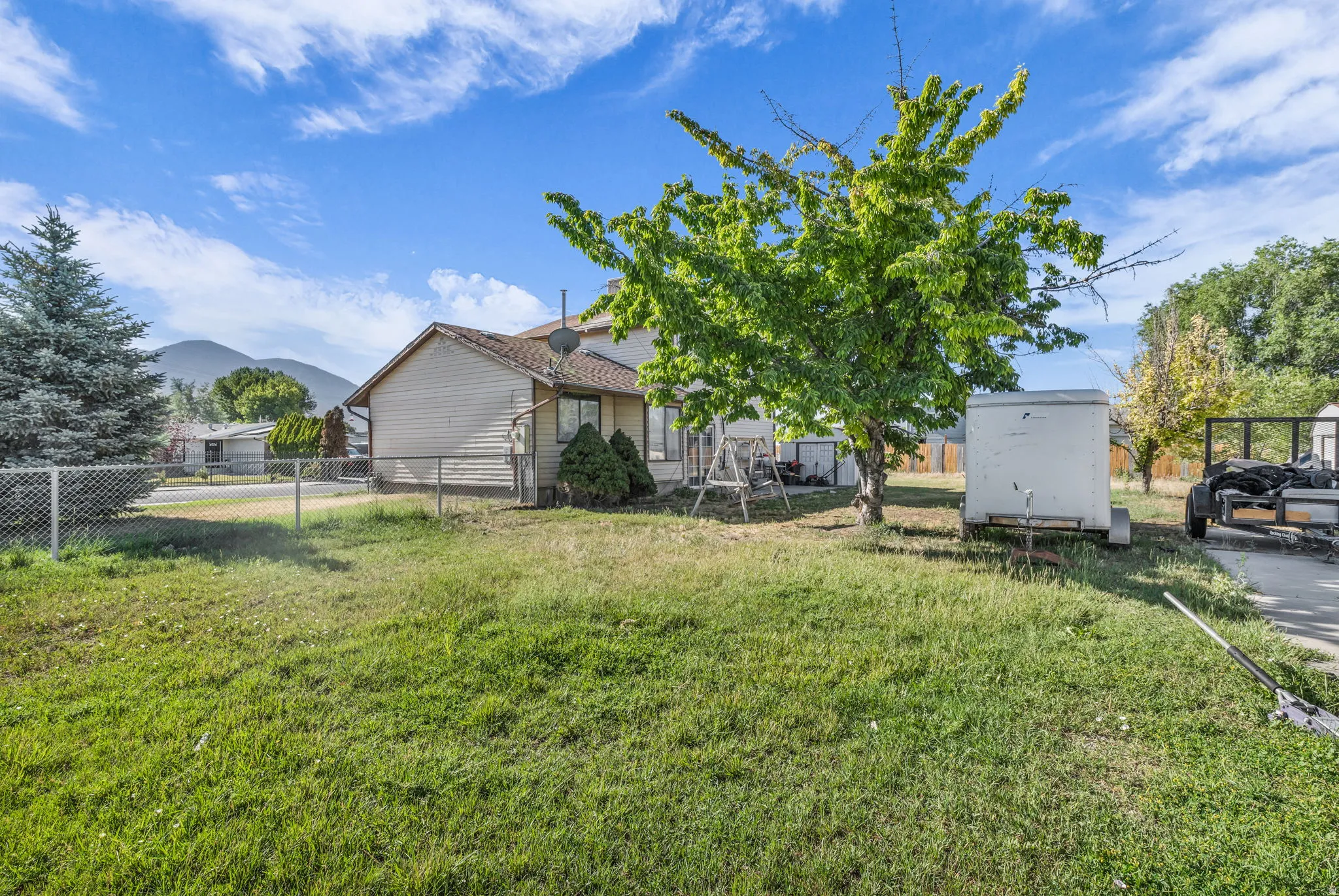 Expansive grassy yard area with chain-link fencing and mature trees
