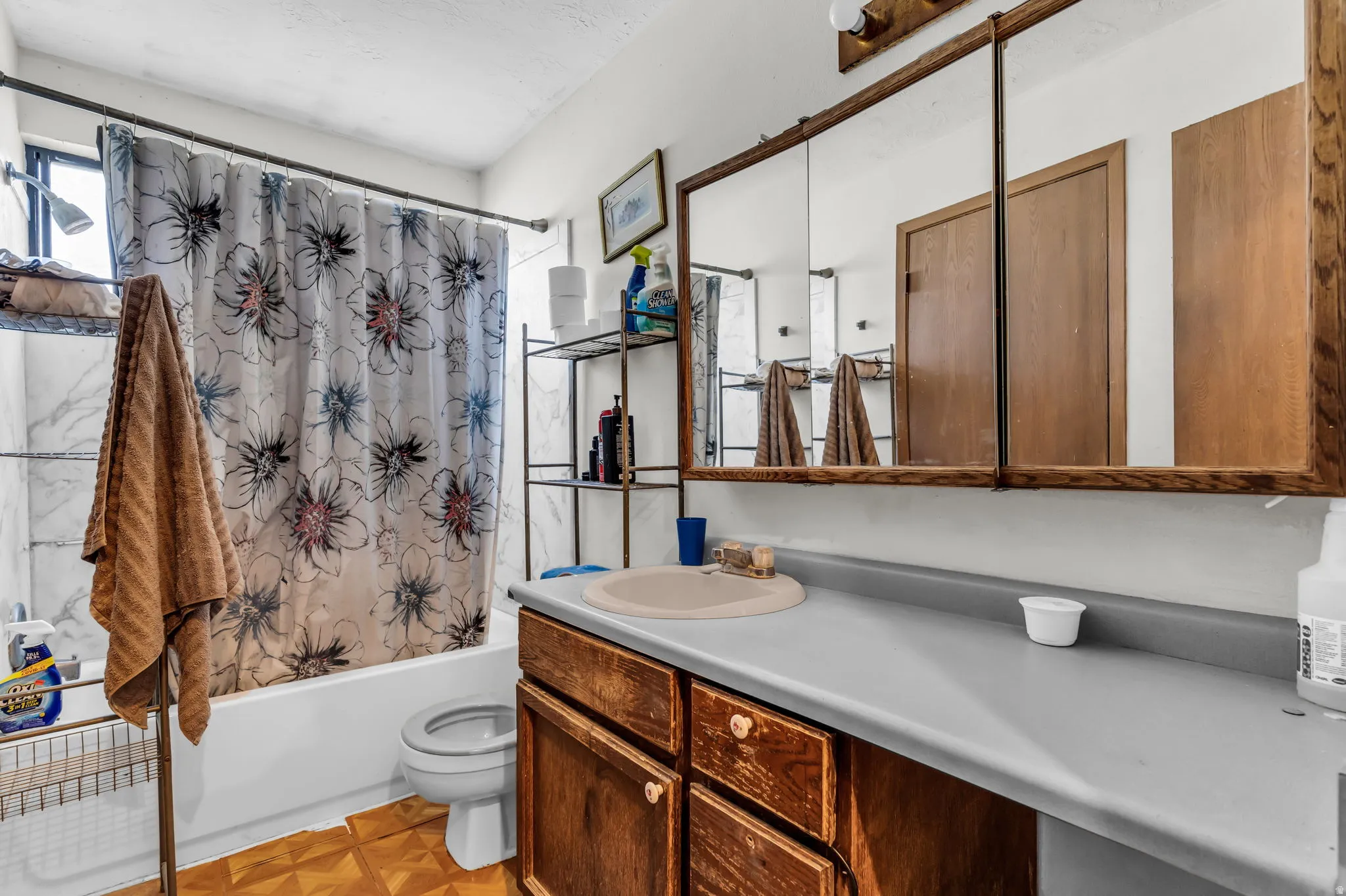 Bathroom featuring a wood-finish vanity with a built-in sink, a wall-mounted mirrored medicine cabinet, a full-size bathtub with a shower, and tile-look wall surrounds