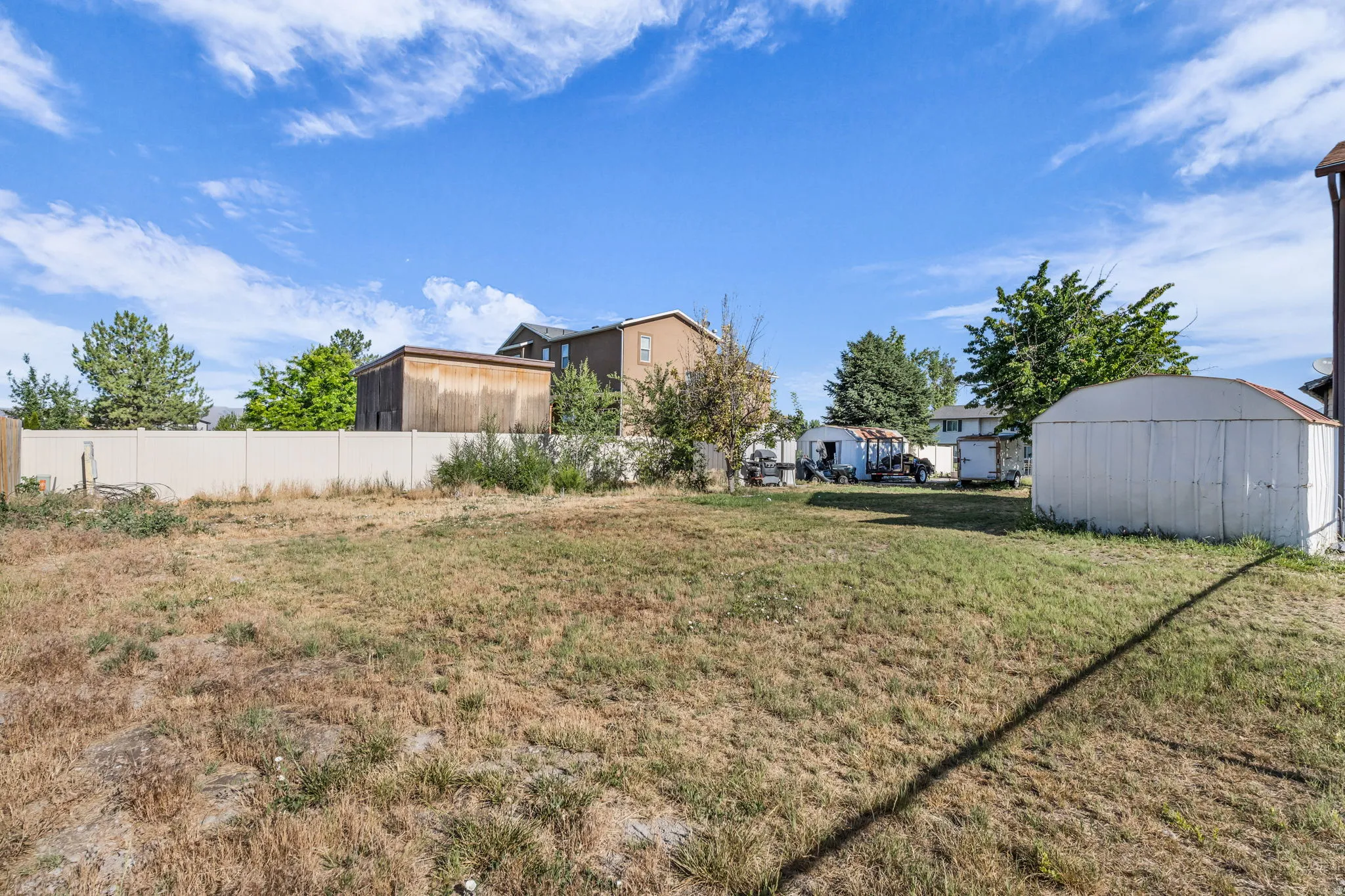 Expansive exterior space featuring a privacy fence, mature trees, and a utility shed