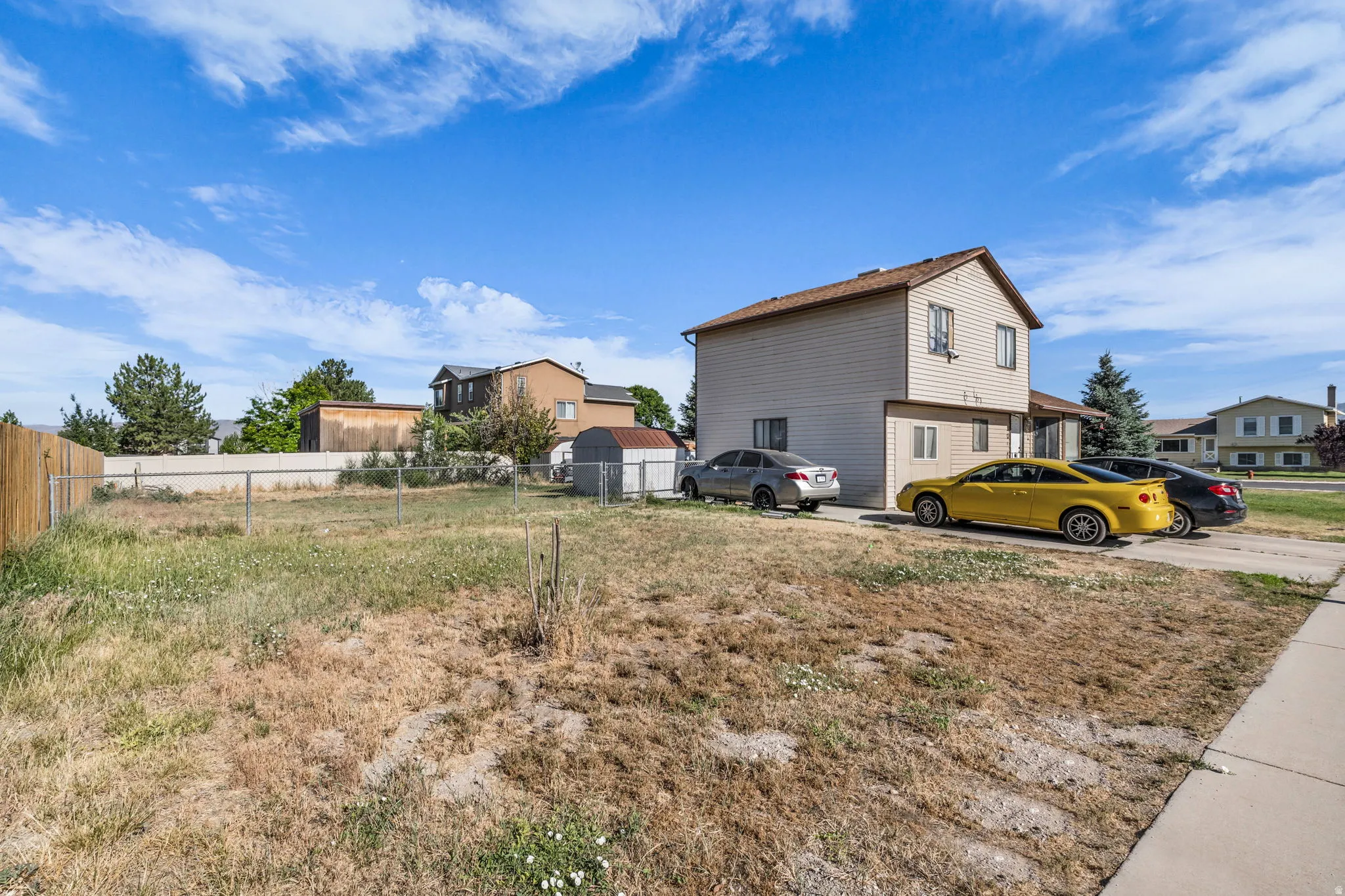 Expansive land parcel featuring a chain-link fence, mature trees, and a gravel driveway