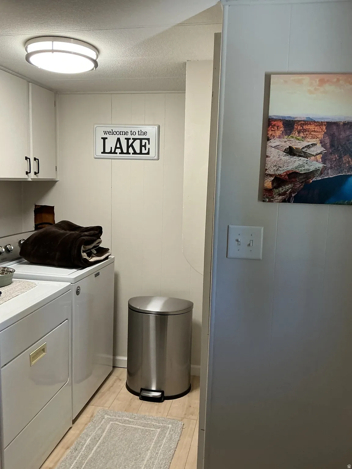 Laundry area featuring light wood-finish flooring, white paneled walls, and built-in cabinetry with dark hardware