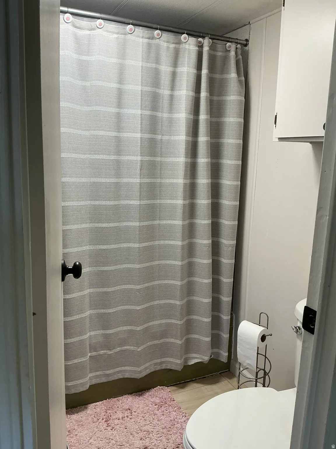 Compact bathroom featuring a shower area with a white and gray striped shower curtain, a white toilet, and light-colored flooring