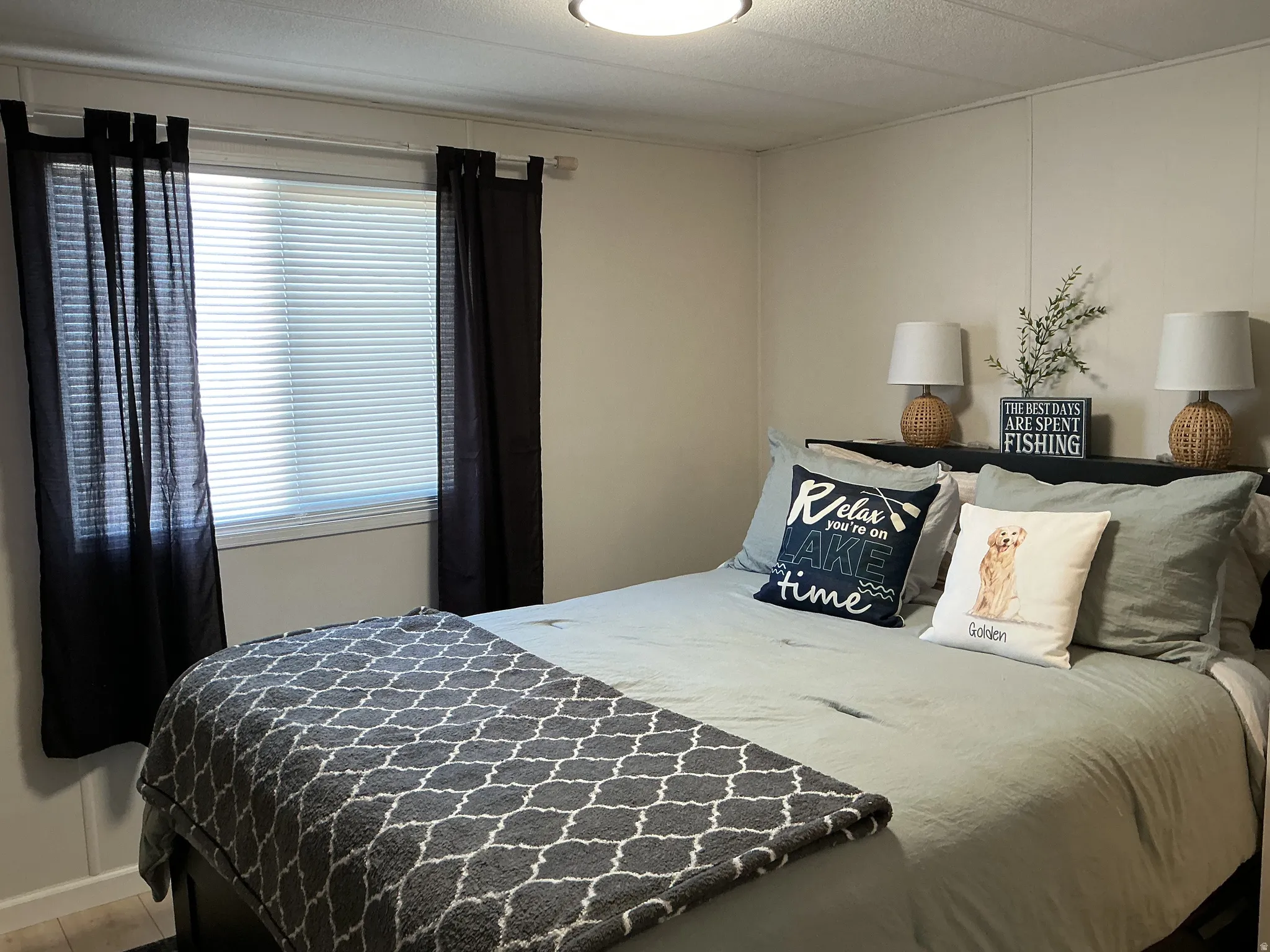 Bedroom featuring a window with blinds, light-toned wall paneling, and a flush-mount ceiling light fixture