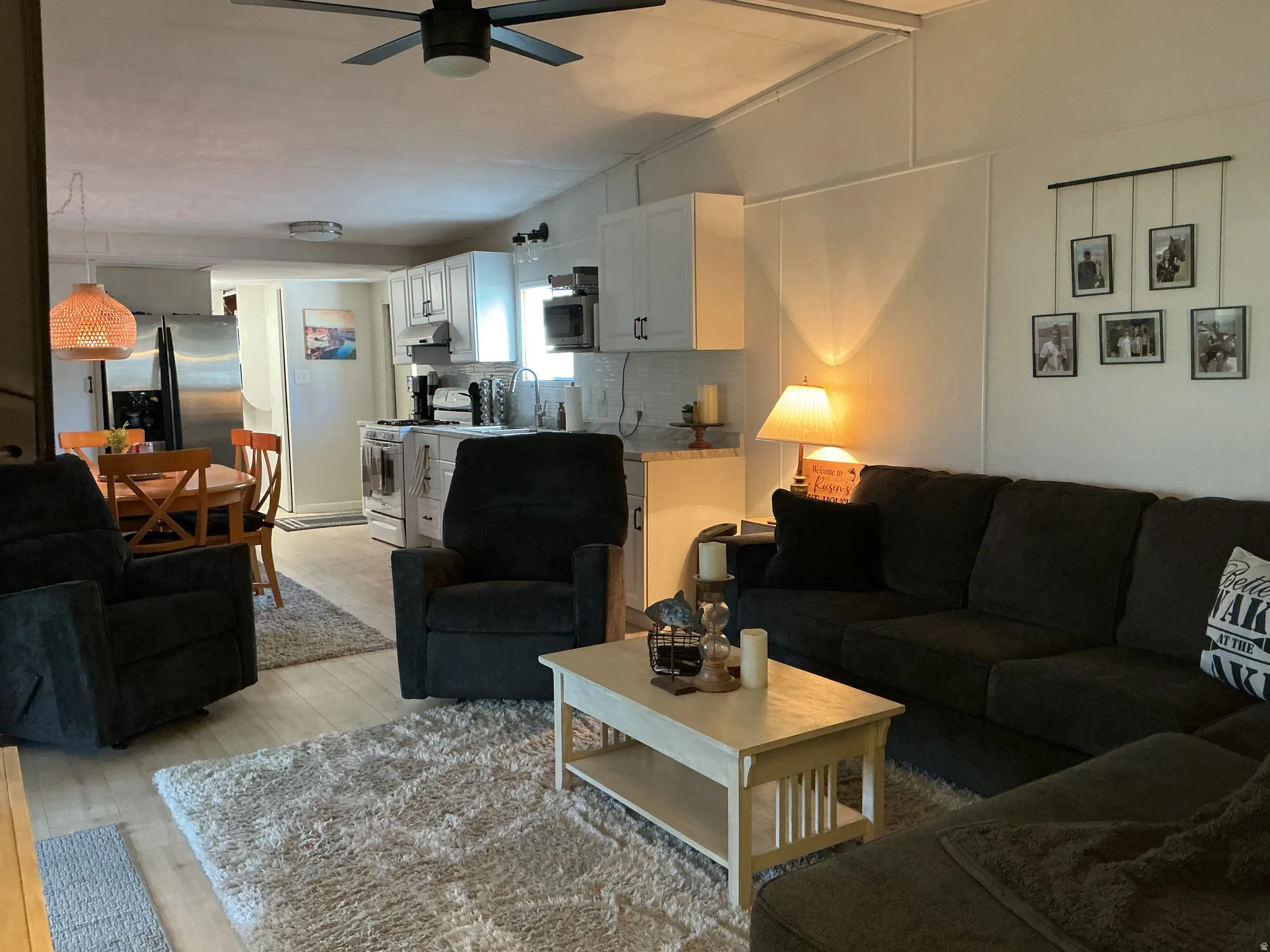 Open-concept living area featuring light wood-finish flooring, a contemporary ceiling fan, white paneled walls, white cabinetry, and stainless steel appliances