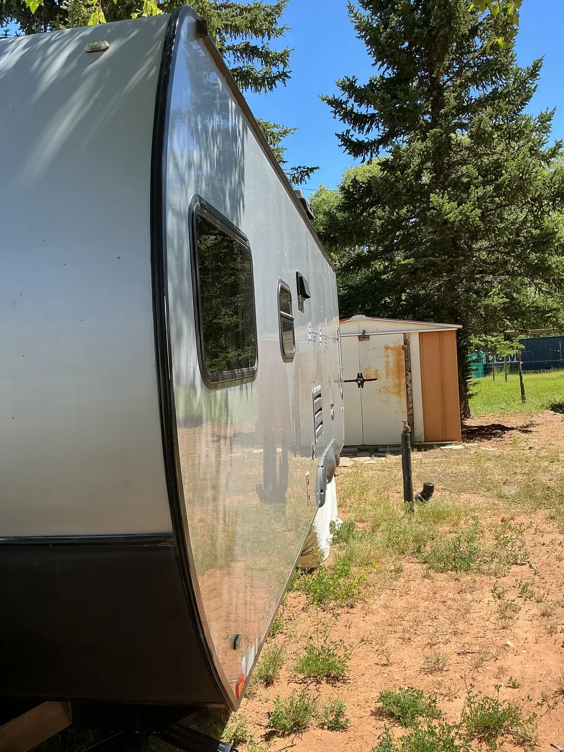 Recreational vehicle exterior featuring a light gray body with dark trim and tinted windows