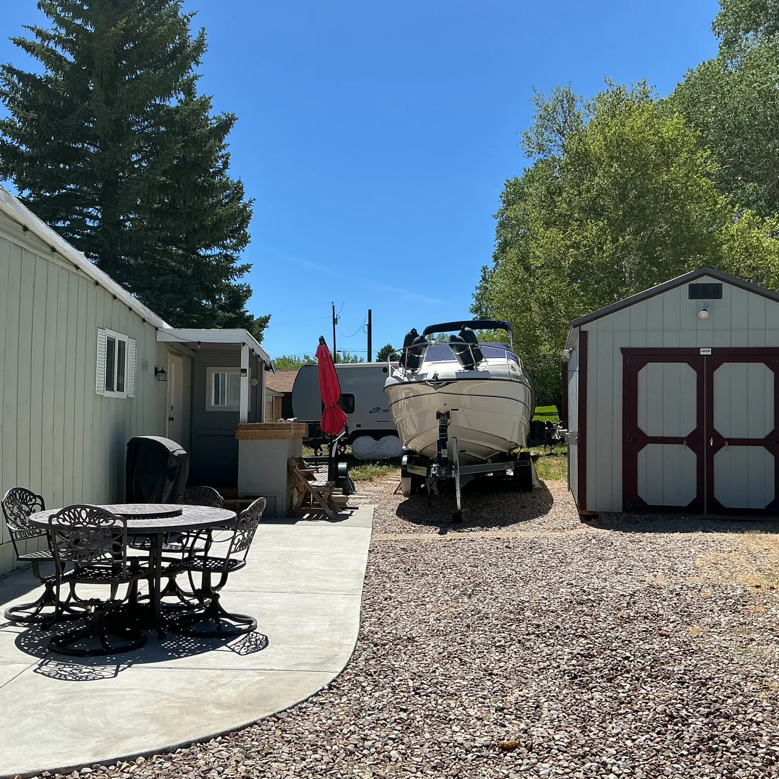 Concrete patio area with a built-in outdoor kitchen, gravel driveway, and a storage shed