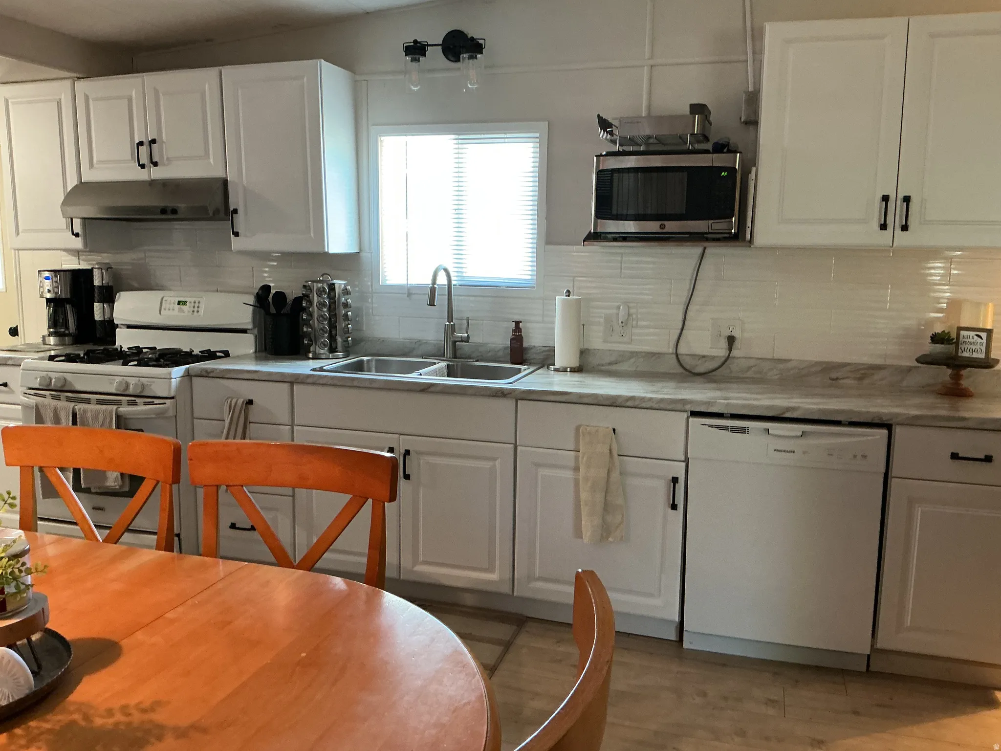 Modern kitchen featuring white shaker cabinetry, stainless steel appliances, a double basin sink, and a white tile backsplash