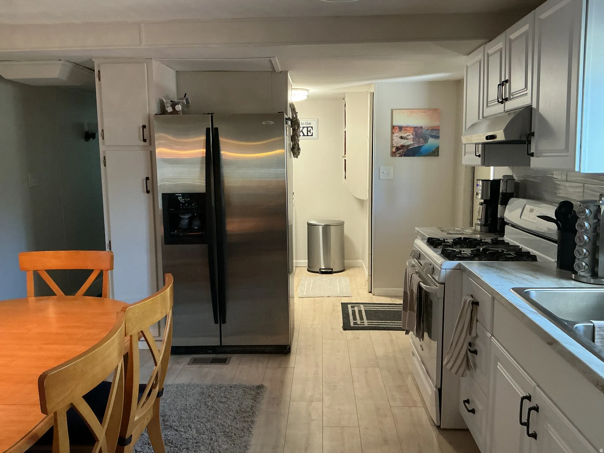 Kitchen featuring light wood-finish flooring, white cabinetry with black hardware, a stainless steel gas range, and a stainless steel French door refrigerator