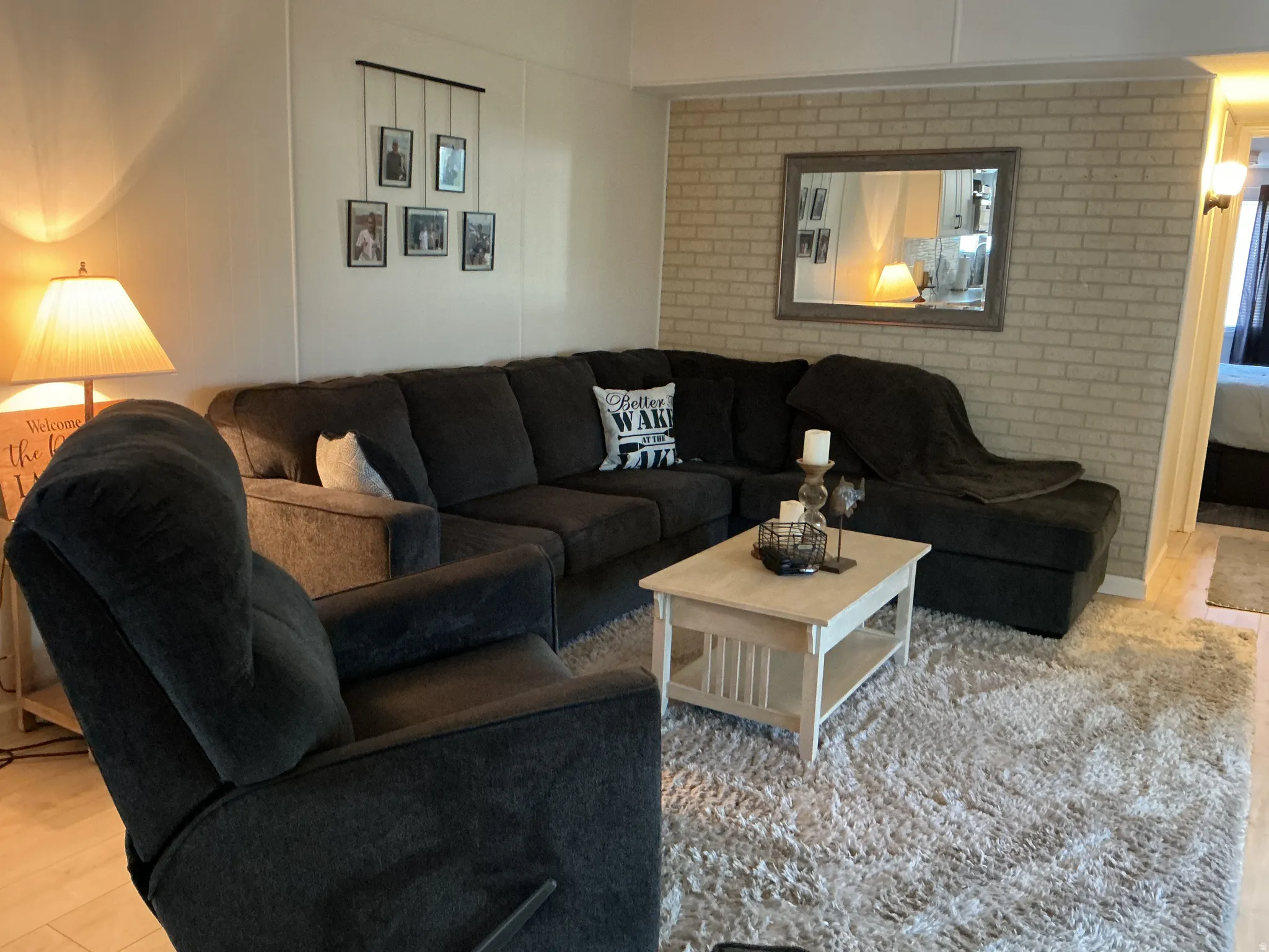 Living area featuring light wood-finish flooring, a neutral brick-patterned accent wall, and a cream-colored area rug