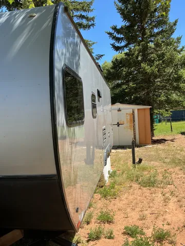 Recreational vehicle exterior featuring a light gray body with dark trim and tinted windows