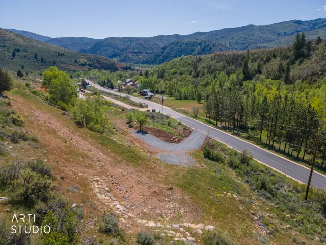Elevated lot featuring a gravel driveway, paved road frontage, and mountainous surroundings with extensive tree coverage