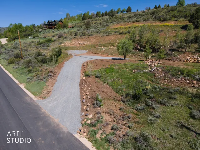 Gravel driveway extending from the paved road, bordered by natural stone accents and rugged terrain